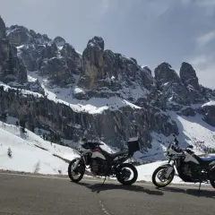 Due moto da enduro parcheggiate su una strada innevata, con imponenti vette delle valli bergamasche sullo sfondo.