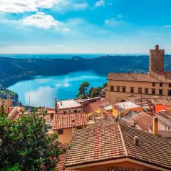 Panoramica dei Castelli Romani in moto: tetti rossi, un lago blu e un cielo terso.