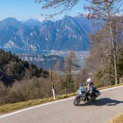 Un motociclista si gode un giro in moto sul Lago di Garda, con montagne maestose e un villaggio sullo sfondo.