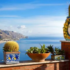 Balcone fiorito con vista sul mare, tra i posti più belli della Sicilia. Cactus e vasi decorati con teste di moro.