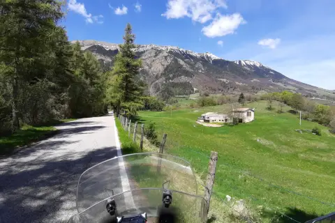 Strada di montagna, un'avventura in moto verso la punta veleno. Paesaggio verdeggiante, montagne innevate e cielo azzurro.