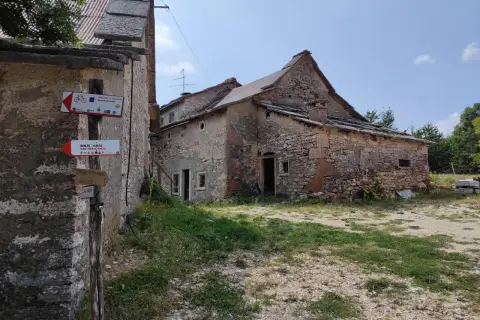 Un vecchio parparo in pietra, con tetto in lamiera e tegole, mostra cartelli per sentieri escursionistici e ciclabili.