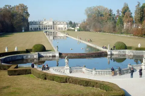 Un'imponente villa con un lungo specchio d'acqua e giardini curati, che ricorda le ville palladiane.