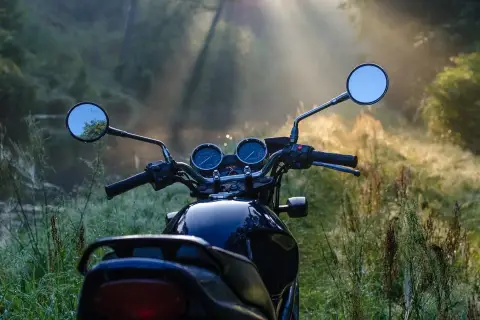 Manubrio di moto scura in un prato nebbioso, pronto per esplorare i borghi lombardia in moto all'alba.