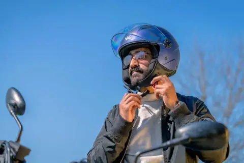 Uomo con casco moto blu, occhiali e barba, che allaccia il sottogola. Ideale per chi cerca una tabella misure casco moto.