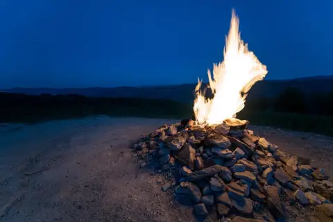 Fuoco acceso su un cumulo di pietre, con le colline del monte Busca sullo sfondo al crepuscolo.