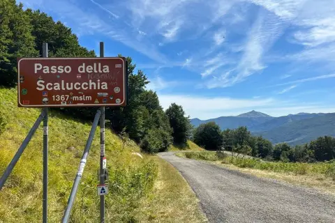 Cartello stradale indica Passo della Scalucchia a 1367 metri. La strada sale tra alberi e montagne sullo sfondo.
