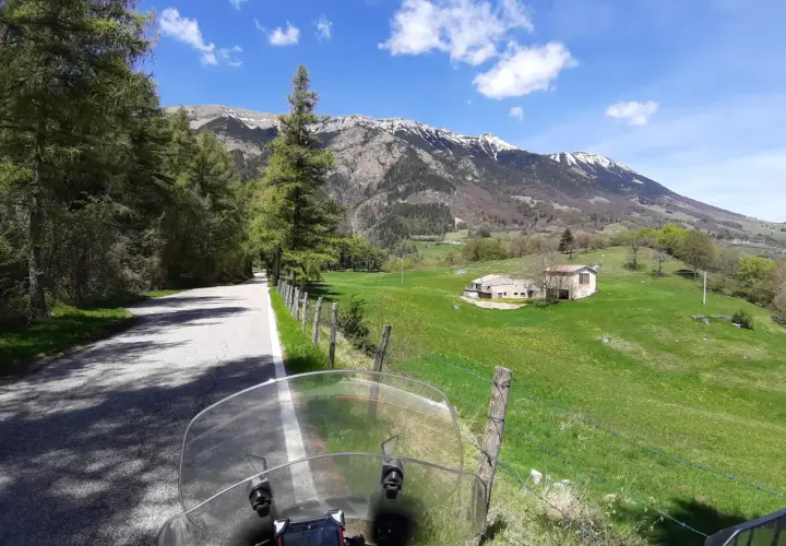 Strada di montagna, un'avventura in moto verso la punta veleno. Paesaggio verdeggiante, montagne innevate e cielo azzurro.