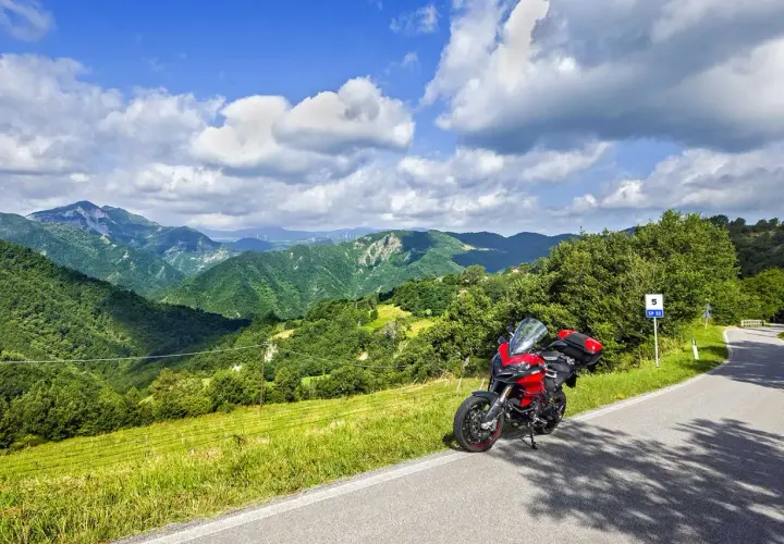 Ducati rossa ferma sul ciglio della strada statale 67, con un panorama mozzafiato di colline verdi e cielo azzurro.
