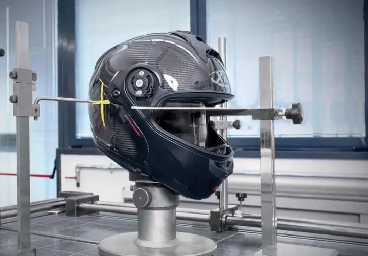 Casco da moto in carbonio sottoposto a test per l'omologazione, con strumenti di misurazione che ne verificano la resistenza e la sicurezza.