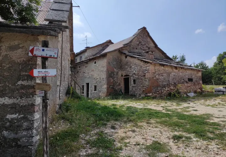 Un vecchio parparo in pietra, con tetto in lamiera e tegole, mostra cartelli per sentieri escursionistici e ciclabili.