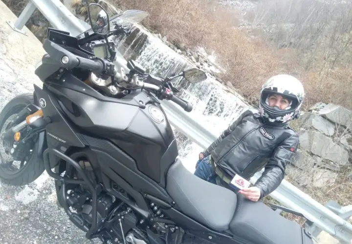 Panoramica Zegna moto con motociclista in giacca di pelle, accanto a una cascata.