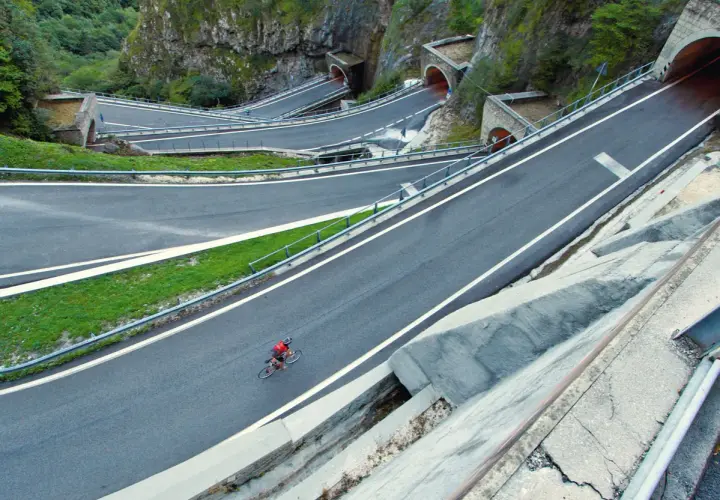 Ciclista solitario affronta i tornanti del passo Bidibidì, tra gallerie scavate nella roccia e panorami mozzafiato.