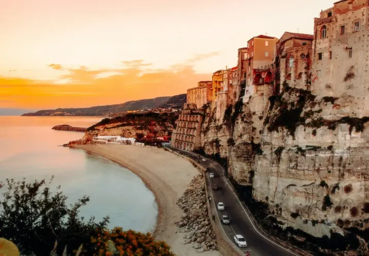 Tramonto mozzafiato sulla costa, con case aggrappate alla scogliera. Un sogno di **Calabria in moto**.