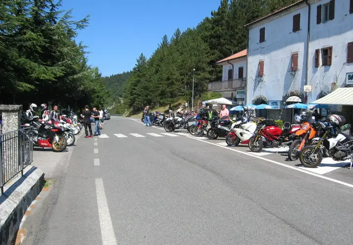 Gruppo di motociclisti in sosta lungo la strada statale 67 Tosco Romagnola, con moto parcheggiate e un hotel sullo sfondo.
