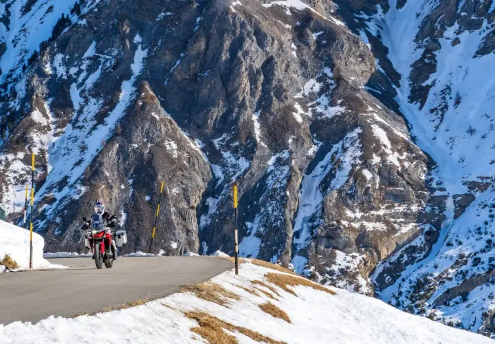 Motociclista su strada innevata tra le montagne, un viaggio da Bolzano a Livigno.