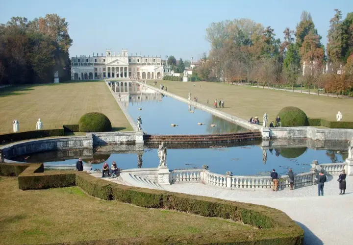 Un'imponente villa con un lungo specchio d'acqua e giardini curati, che ricorda le ville palladiane.