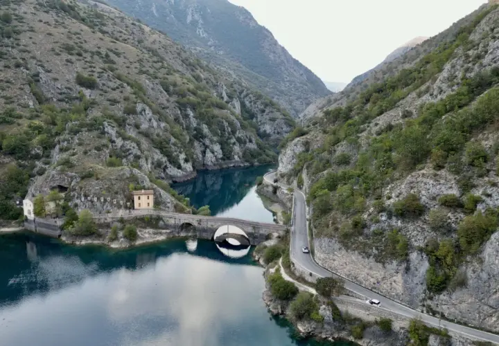 Le gole del Sagittario a Scanno, con il lago turchese, il ponte ad arco e la strada panoramica che serpeggia tra le montagne.