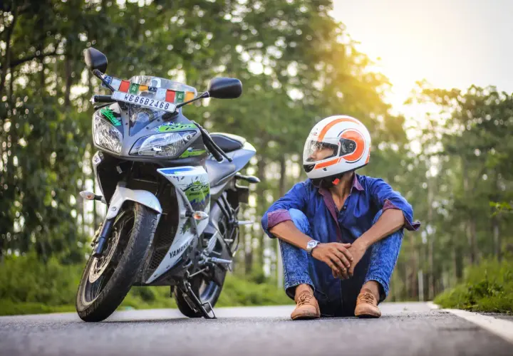 Giovane con casco arancione e bianco, seduto accanto alla sua moto. Spera di allargare il casco stretto per un viaggio più comodo.
