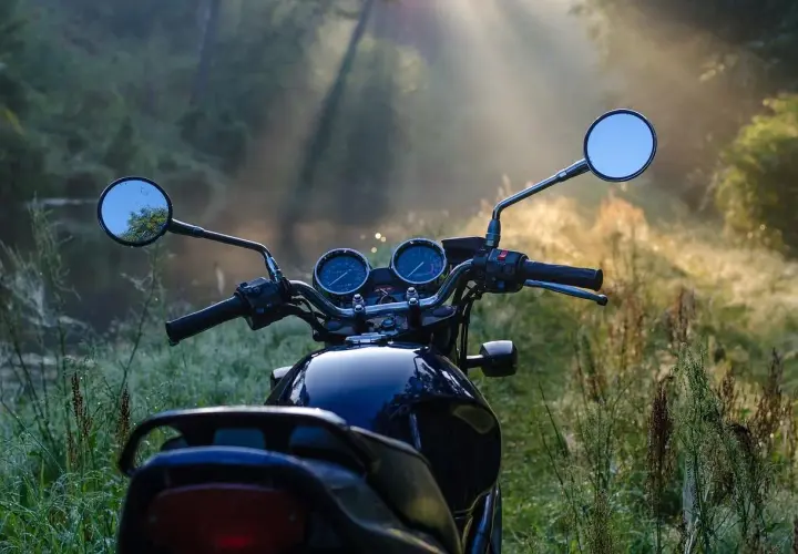 Manubrio di moto scura in un prato nebbioso, pronto per esplorare i borghi lombardia in moto all'alba.