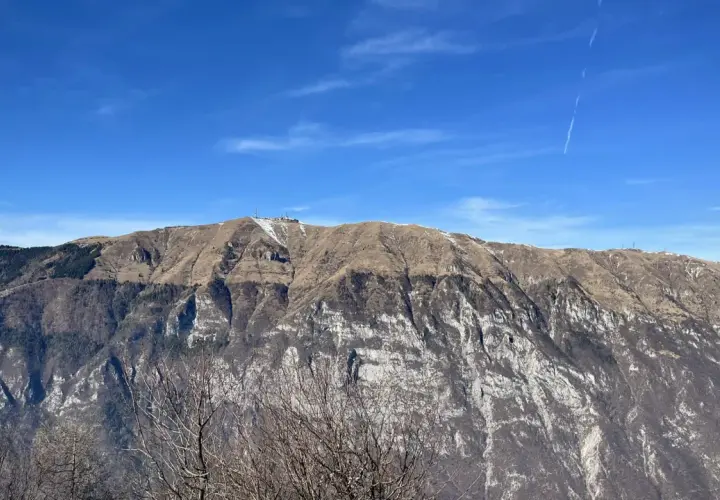 Vetta del monte Pizzoc con neve residua, pendii bruni e rocce bianche sotto un cielo azzurro con scie di aerei.
