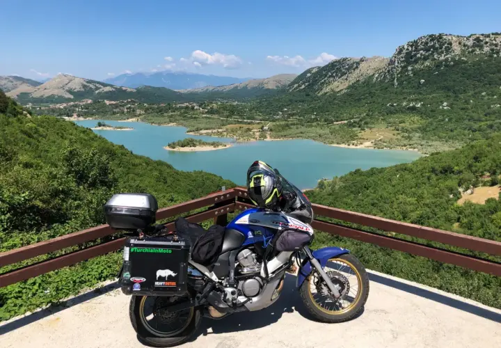 Moto pronta per esplorare gli Appennini, con un lago turchese e montagne verdi sullo sfondo. #AppenniniInMoto