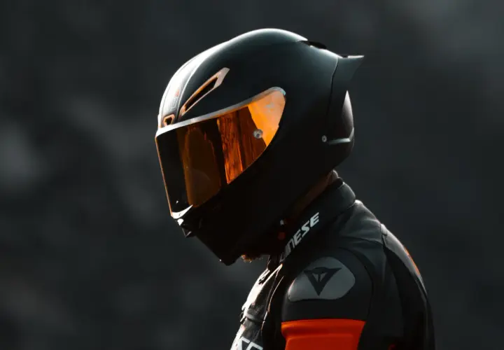 Un motociclista indossa un casco integrale nero con visiera arancione riflettente, pronto per la pista.