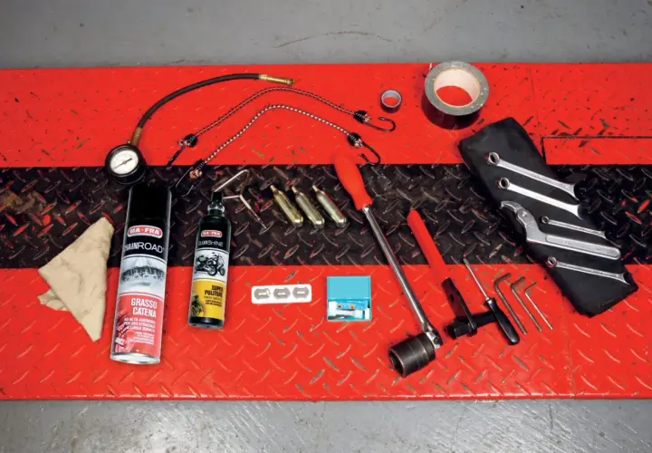 Kit di attrezzi da portare in moto: grasso catena, pulitore, chiavi, brugole, compressore portatile e nastro adesivo.