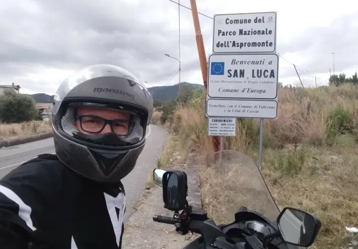 Sila in moto, selfie con casco e giacca da motociclista, vicino ai cartelli del Parco Nazionale dell'Aspromonte e di San Luca.