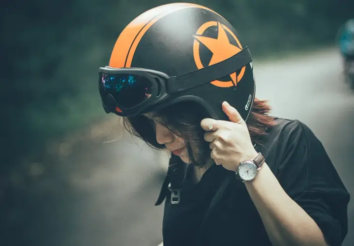 Ragazza con casco da moto nero e arancione, occhiali riflettenti. Dove mettere il casco della moto? Forse qui, prima di partire.
