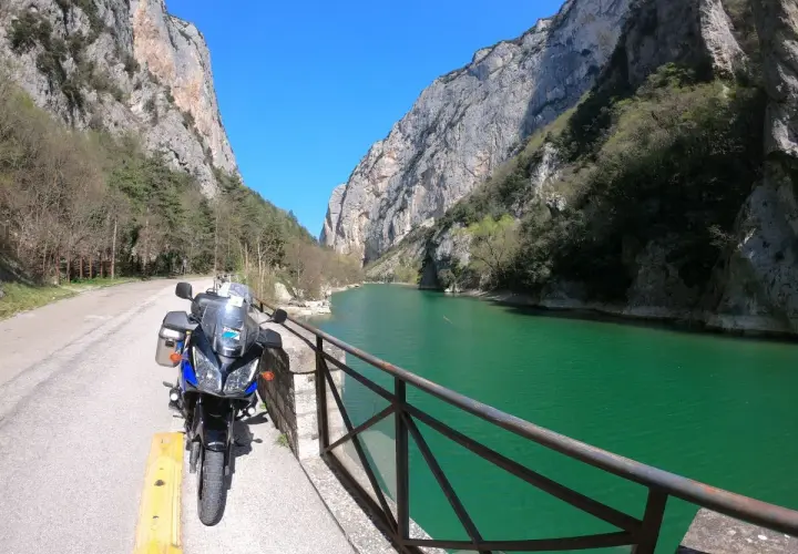 Moto parcheggiata lungo la strada panoramica delle Gole del Furlo, con il fiume color smeraldo e le imponenti pareti rocciose.