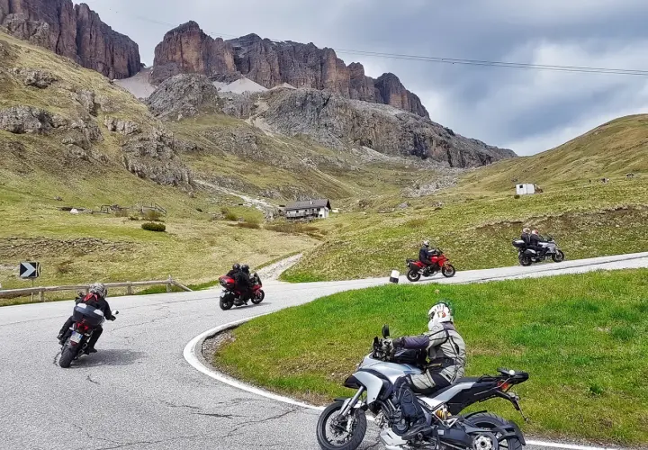 Motociclisti in gruppo affrontano le curve del passo della Cappelletta, tra verdi pendii e imponenti pareti rocciose.
