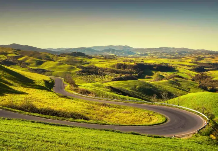 Strada volterrana serpeggiante tra dolci colline verdi sotto un cielo limpido.