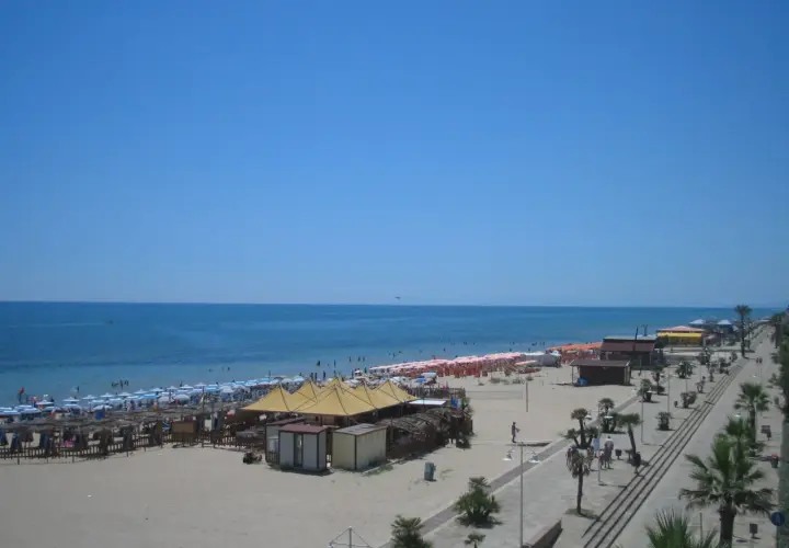Spiaggia affollata a Metaponto, dove si trova un lido con ombrelloni, lettini e stabilimenti balneari. Il mare azzurro e il cielo limpido invitano al relax.