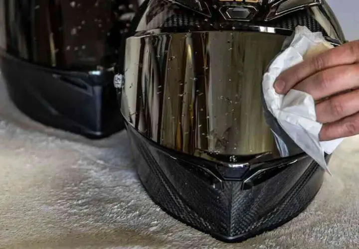 Mano che pulisce la visiera del casco con un panno bianco, rimuovendo insetti e sporco per una guida sicura.