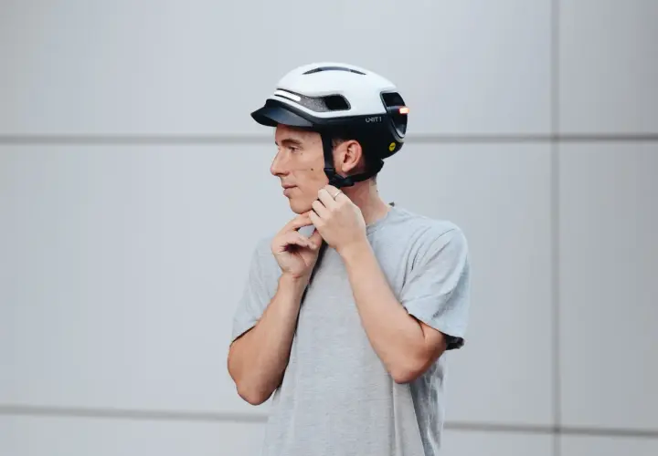 Uomo con casco bianco e nero, che regola gli spallacci. Le taglie caschi sono fondamentali per la sicurezza.