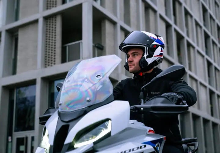 Motociclista con casco modulare, che può essere jet o integrale, pronto a partire con la sua moto davanti a un edificio moderno.