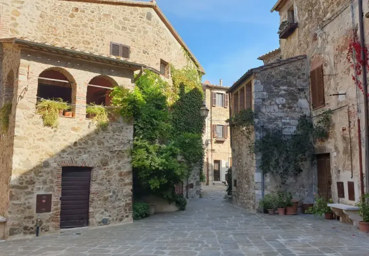 Un vicolo pittoresco a Montemerano, con case in pietra, archi, piante rampicanti e un cielo azzurro. Scopri cosa vedere in questo borgo incantevole.