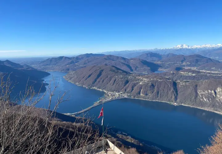 Vista mozzafiato dal balcone d'Italia. Un lago blu intenso abbraccia montagne boscose, con un ponte che attraversa le acque. Perfetto per un viaggio in moto.