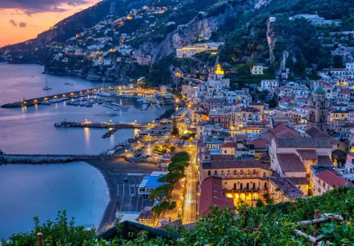 Le luci illuminano le case aggrappate alla costa e il porto turistico. Le strade costiera amalfitana prendono vita al tramonto.