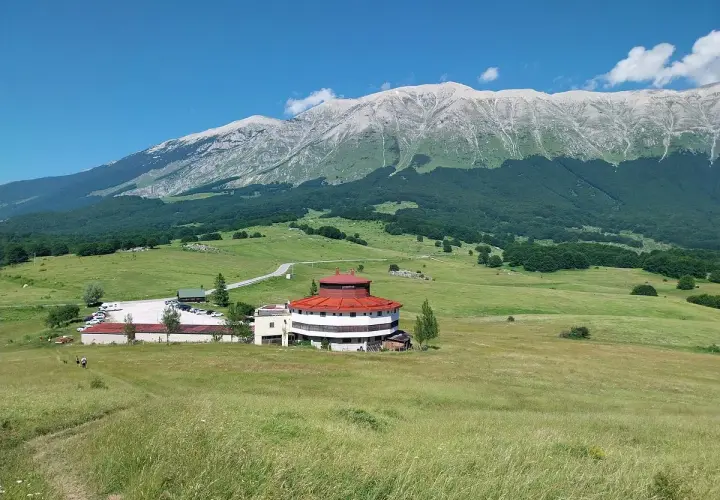 Edificio circolare con tetto rosso e montagne sullo sfondo, al passo San Leonardo.