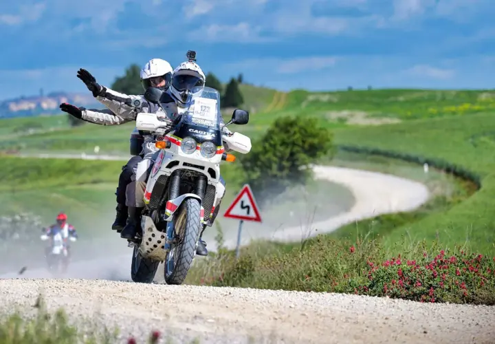 Coppia in moto su sterrato, seguendo una mappa percorso eroica in moto tra colline verdi.