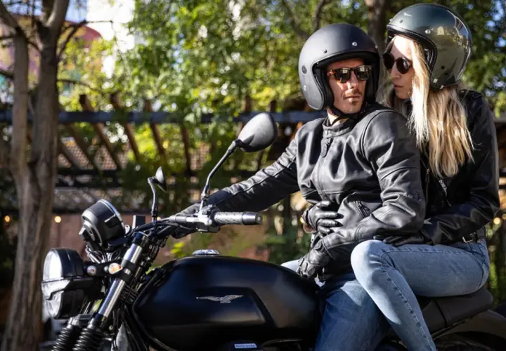 Coppia in moto, lei mostra come vestirsi per andare in moto donna con giacca in pelle e jeans.