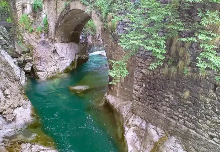 Acqua smeraldo scorre sotto un antico ponte di pietra, creando un'atmosfera suggestiva nell'orrido Val Taleggio.