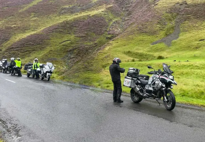Motociclisti in sosta sul passo della Contessa, con moto cariche e un paesaggio collinare verde e viola sullo sfondo.