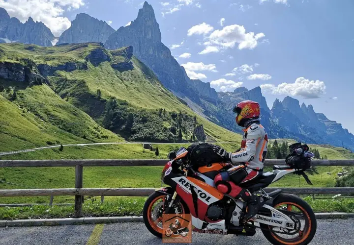Motociclista in tenuta da gara su una Honda Repsol, con lo sfondo delle maestose vette del Passo Cereda.