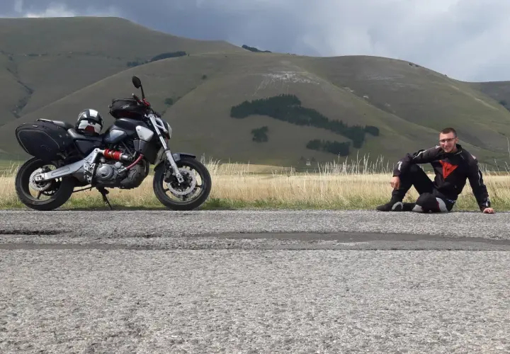 Motociclista in tenuta da gara seduto sul ciglio della strada al passo San Antonio, con la sua moto parcheggiata accanto.