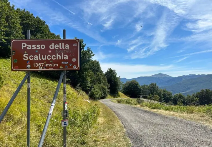 Cartello stradale indica Passo della Scalucchia a 1367 metri. La strada sale tra alberi e montagne sullo sfondo.
