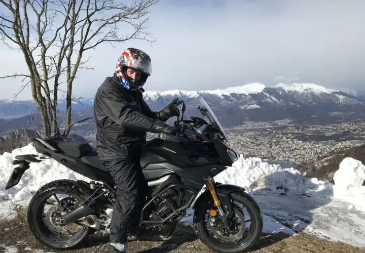 Motociclista con casco stellato su un balcone d'Italia innevato, con vista su montagne e città.