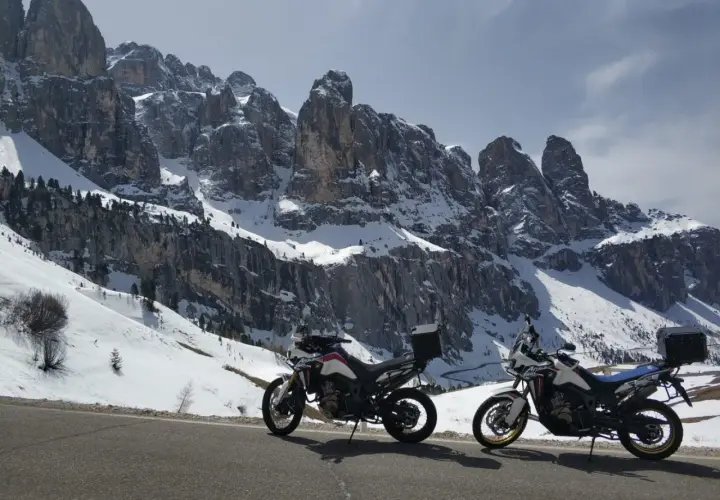 Due moto da enduro parcheggiate su una strada innevata, con imponenti vette delle valli bergamasche sullo sfondo.